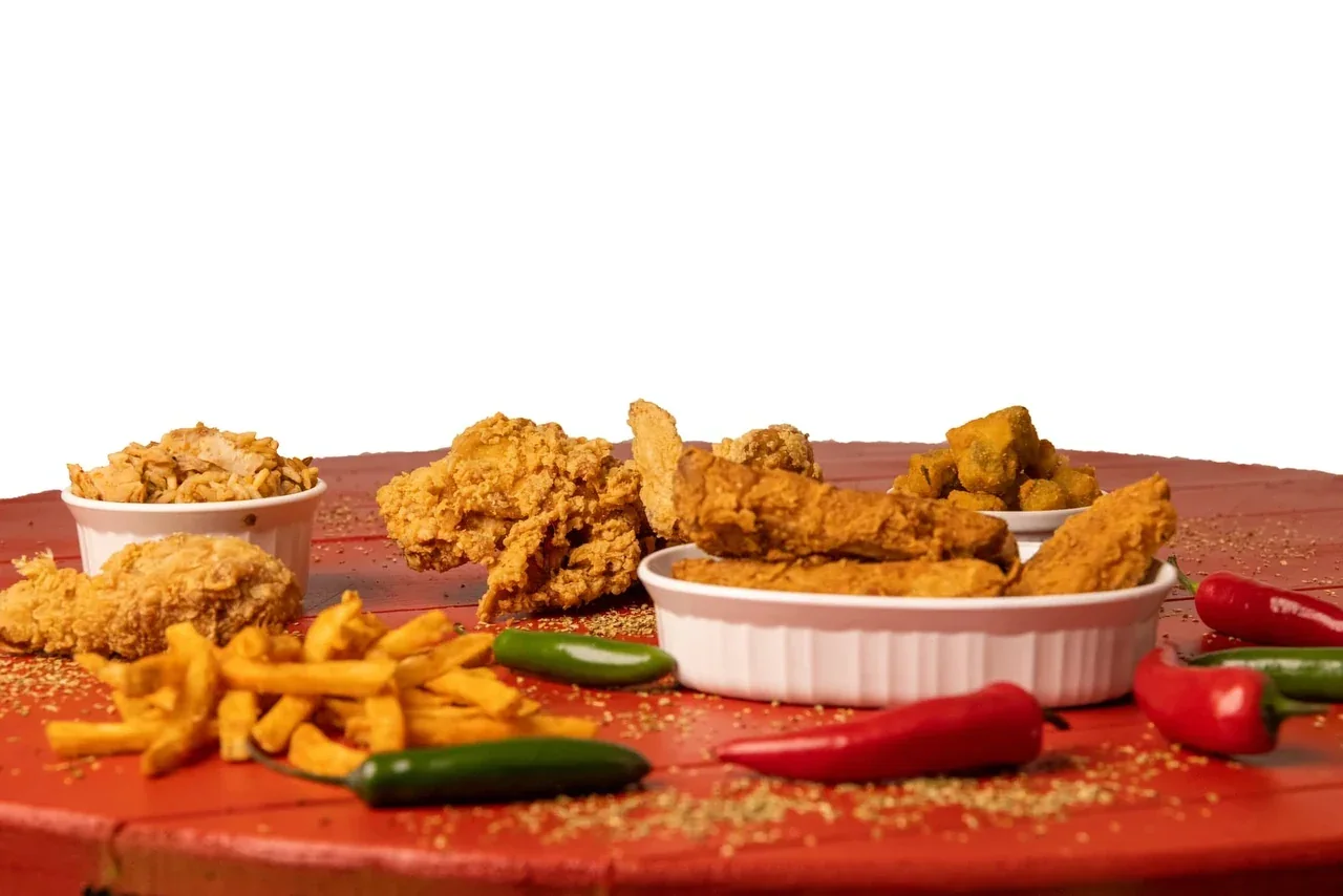 A spread of Creole Fried Chicken, tenders, fries and fresh chillies on a red table